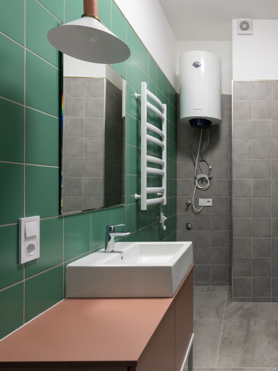 Termo eléctrico blanco colgado en alto en un baño de azulejo verde, junto a la bañera y el lavabo